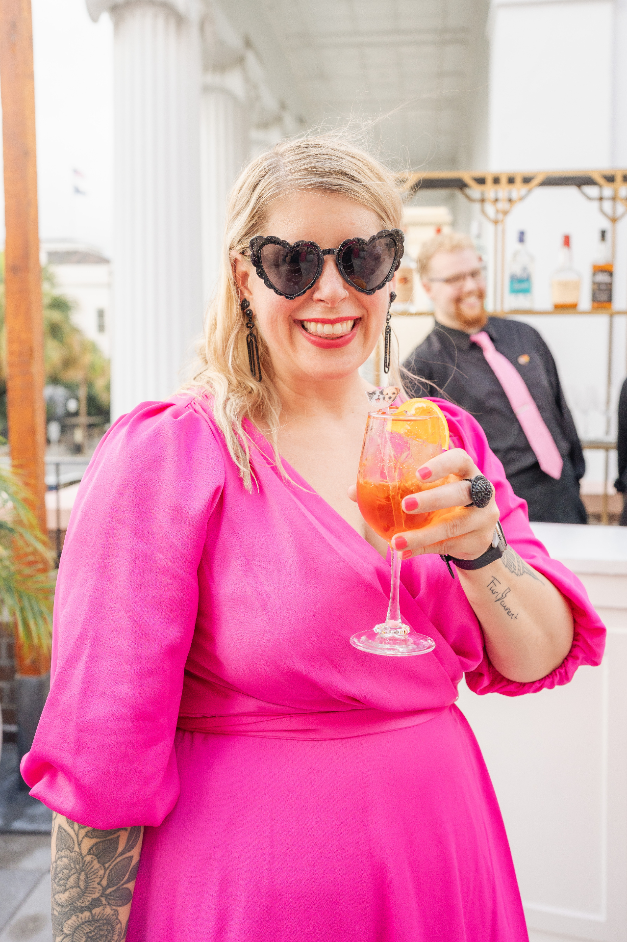 Woman in pink dress and heart-shaped sunglasses holding a cocktail at a wedding